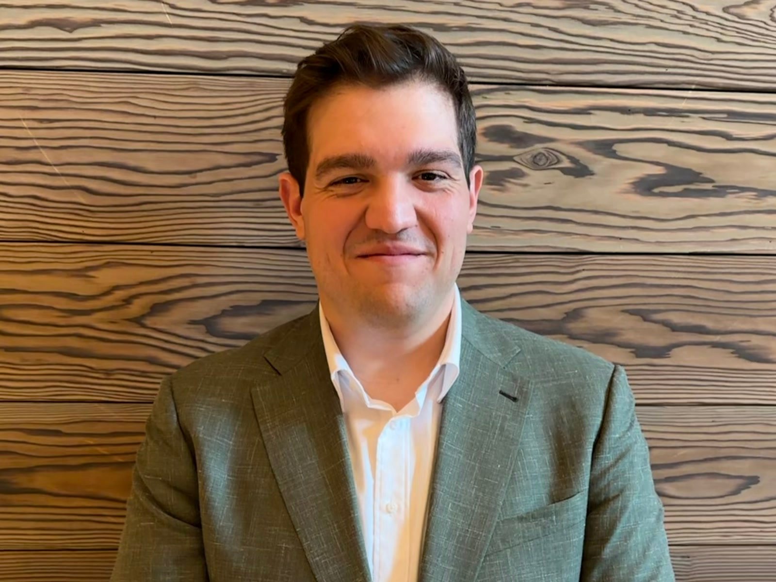 Jason Cruz, smiling in a sage green suit against warm wood paneling